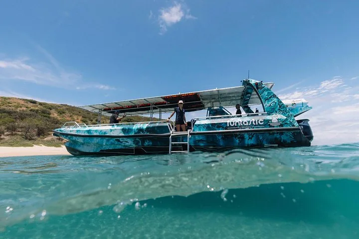 A blue and black tour boat with a sunshade is anchored in shallow water.